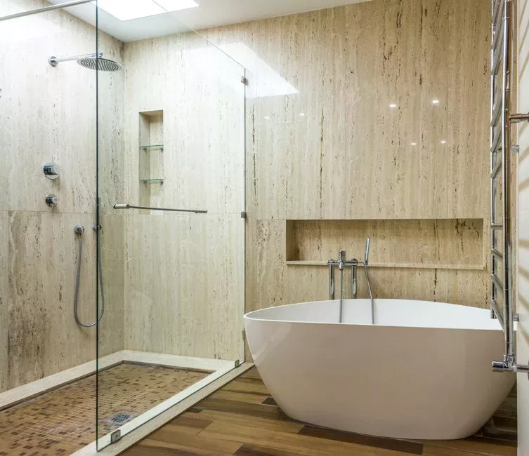 Salle de bain moderne avec revêtement en travertin, douche vitrée et baignoire, illustrant une rénovation avec pierre naturelle.