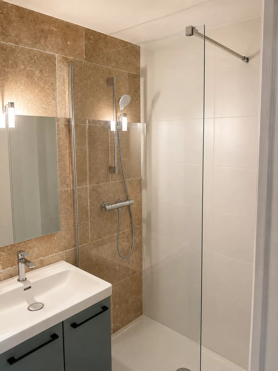 Vue d'ensemble de la salle de bain rénovée à Bormes-les-Mimosas : meuble vasque, douche en travertin et carrelage blanc 30x90.