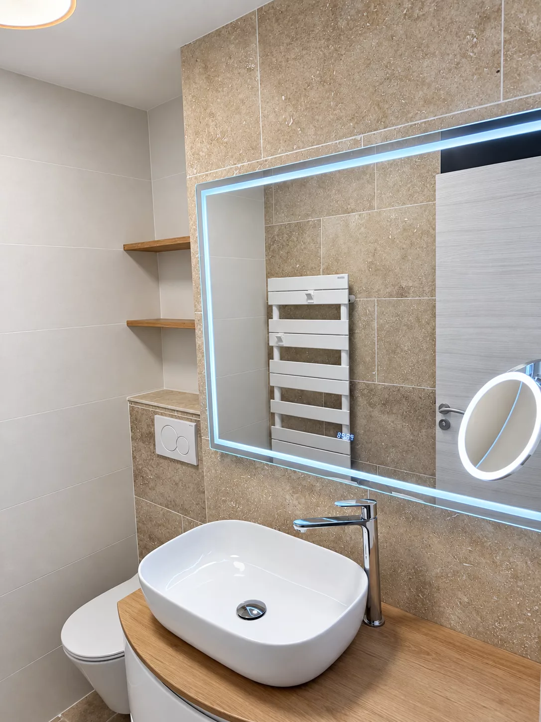 Vasque à poser blanche et meuble en bois clair, sous le miroir LED rétroéclairé.