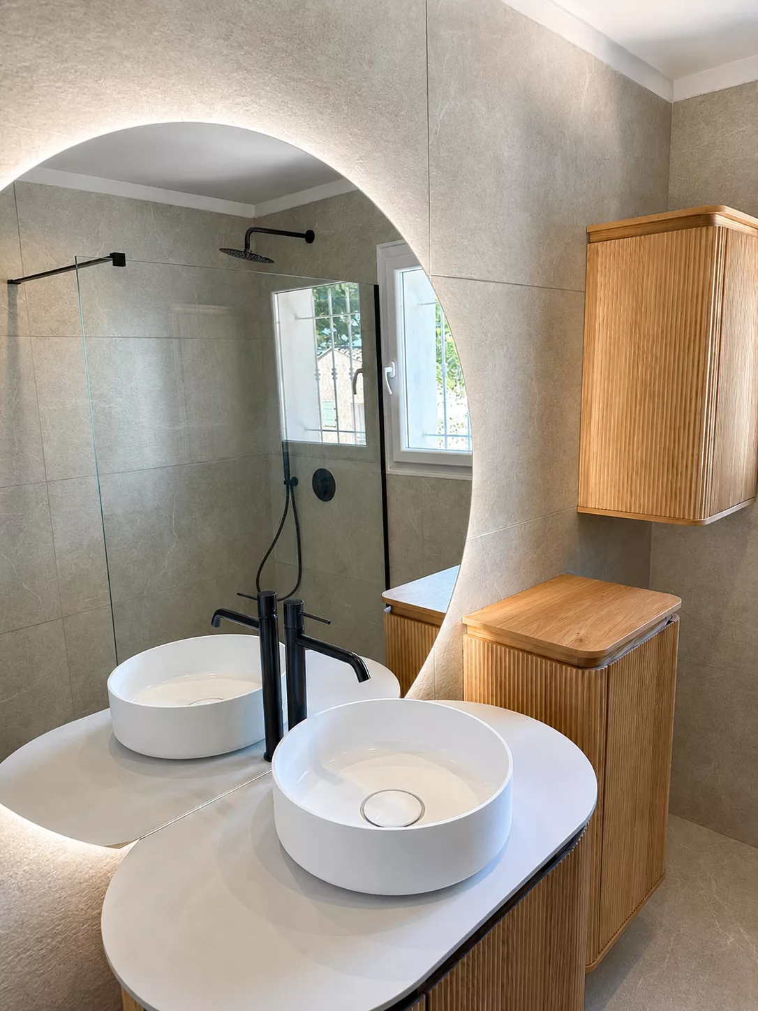 Vue d'ensemble de la salle de bain rénovée à Bandol : double vasque, meuble bois cannelé et douche à l'italienne.