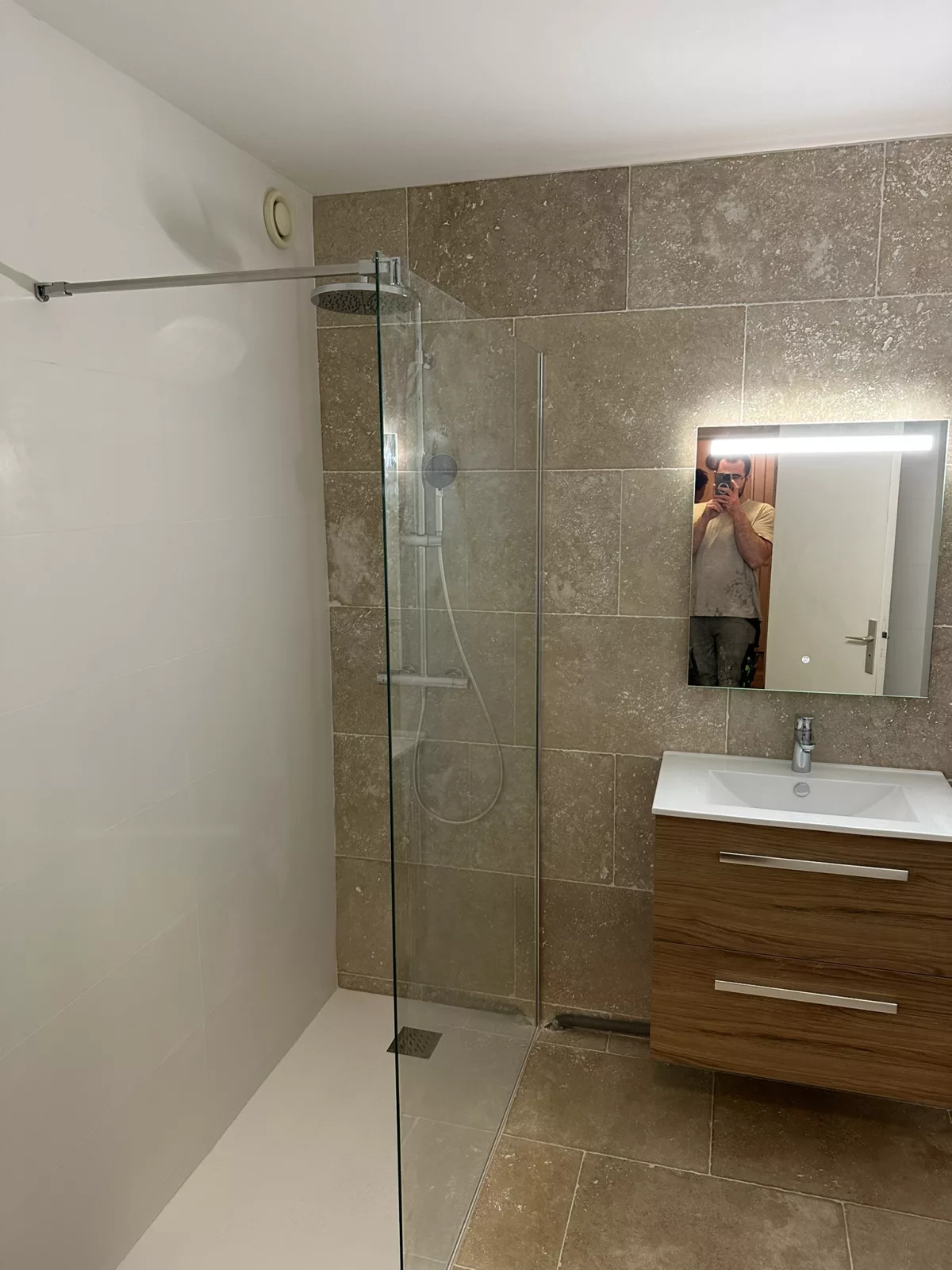 Douche à l'italienne en travertin véritable avec paroi vitrée fixe et meuble vasque en bois, rénovation salle de bain à Hyères.