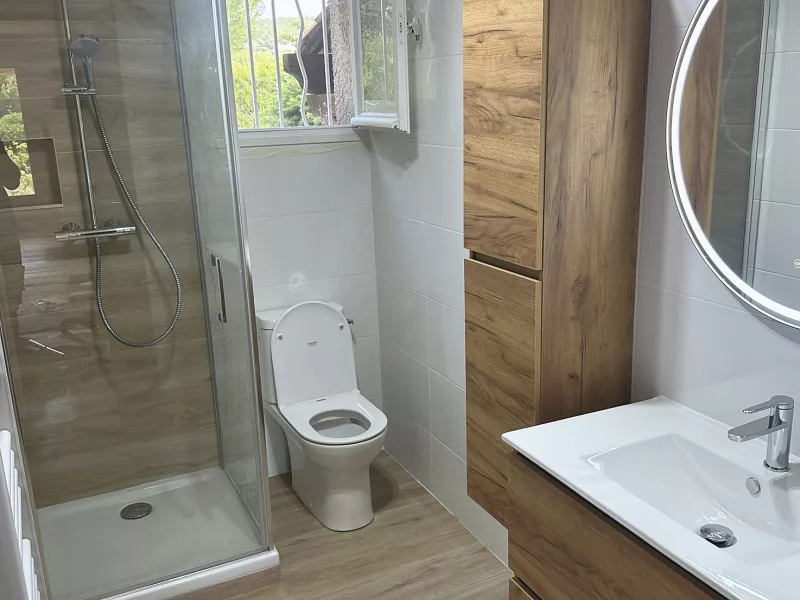 Vue d'ensemble de la salle de bain rénovée à Saint-Cyr-sur-Mer : douche à l'italienne, WC et meuble vasque en bois.