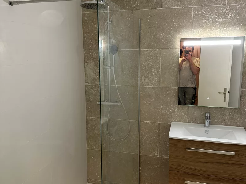 Douche à l'italienne en travertin véritable avec paroi vitrée fixe et meuble vasque en bois, rénovation salle de bain à Hyères.
