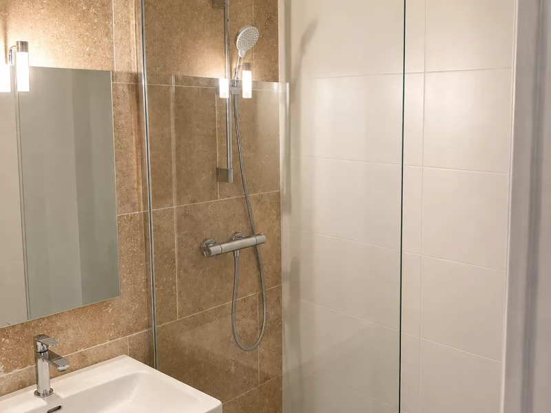 Vue d'ensemble de la salle de bain rénovée à Bormes-les-Mimosas : meuble vasque, douche en travertin et carrelage blanc 30x90.