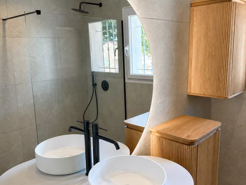 Vue d'ensemble de la salle de bain rénovée à Bandol : double vasque, meuble bois cannelé et douche à l'italienne.