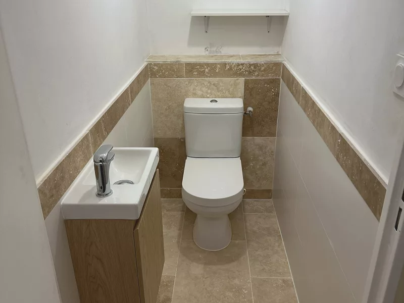 WC indépendants rénovés à Toulon avec frise en travertin et meuble vasque en bois.