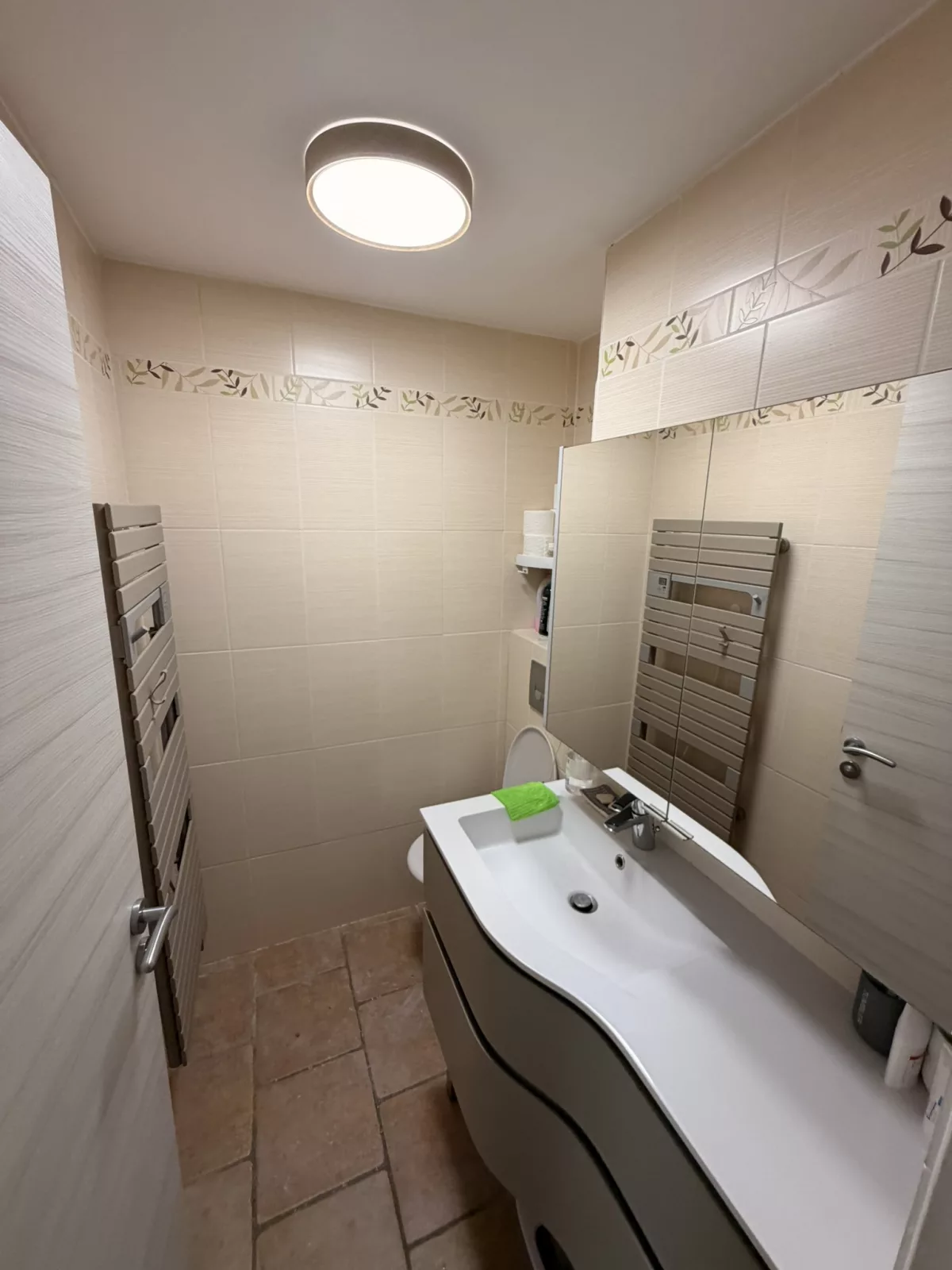 Vue d'ensemble avant travaux : carrelage beige à frise florale et sèche-serviettes vieillissant.