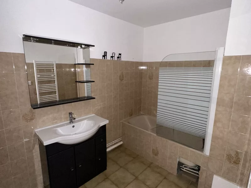 Salle de bain vétuste avant rénovation : ancien carrelage beige, baignoire avec pare-douche et meuble vasque à remplacer.