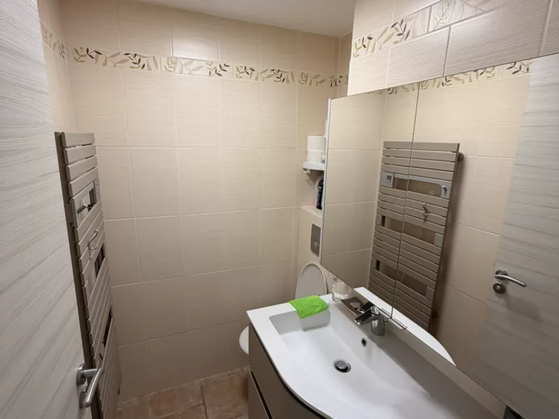 Vue d'ensemble avant travaux : carrelage beige à frise florale et sèche-serviettes vieillissant.