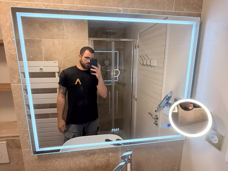 Autoportrait de l'artisan dans le miroir, offrant une vue d'ensemble de la douche et du meuble vasque.