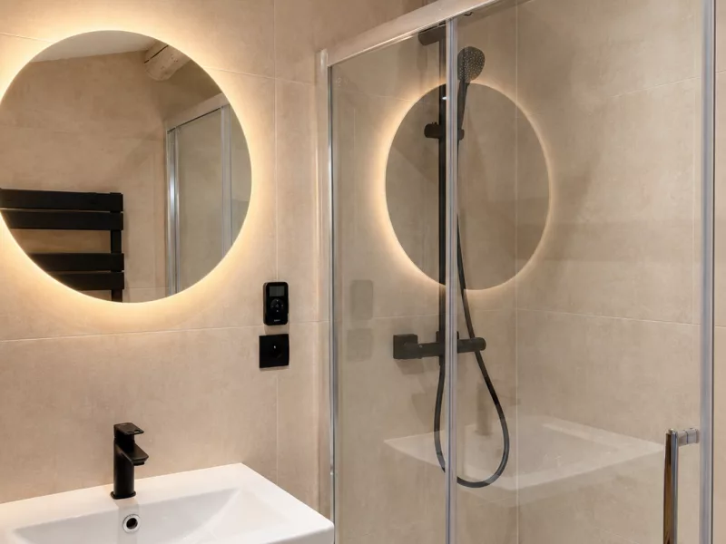 Meuble vasque en bois avec miroir rond rétroéclairé et poutres apparentes, salle de bain rénovée à Aix-en-Provence.