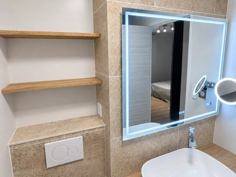 WC suspendu et plaque de commande Geberit, intégrés dans la niche habillée de travertin.