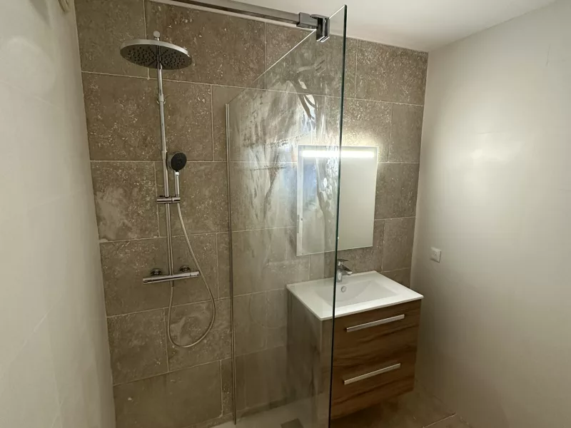 Colonne de douche avec pluie de douche et douchette sur mur en travertin, rénovation salle de bain à Hyères.