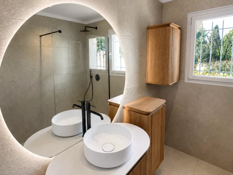 Double vasque à poser sur meuble en bois cannelé avec miroir rond rétroéclairé LED, rénovation salle de bain Bandol.
