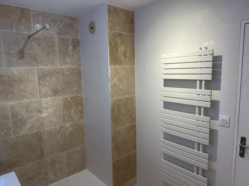 étail des murs en travertin et carrelage blanc 30x90 avec sèche-serviettes électrique, rénovation salle de bain à Toulon.