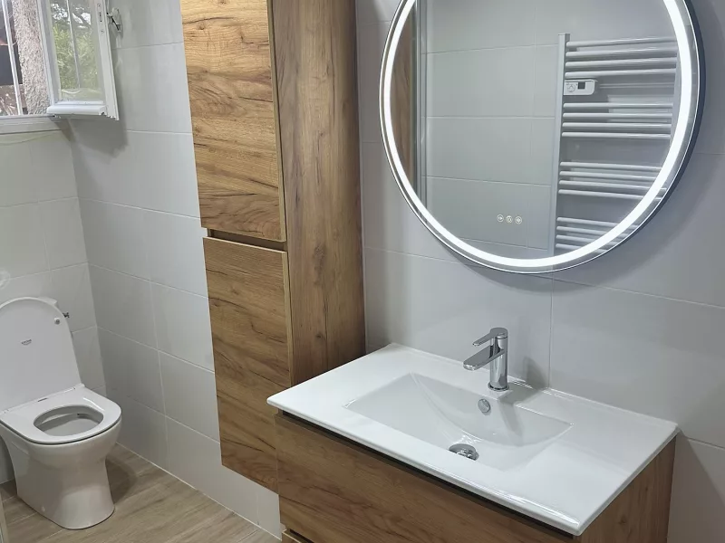 Meuble vasque en bois avec colonne de rangement et miroir rond rétroéclairé LED, rénovation salle de bain à Saint-Cyr-sur-Mer.
