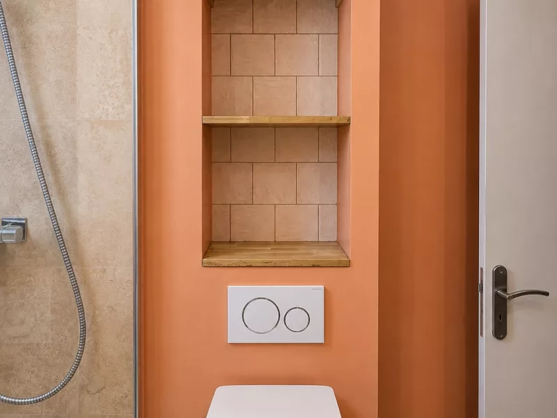Niche de rangement en faïence avec étagères bois au-dessus des toilettes suspendues, plaque de commande Geberit.